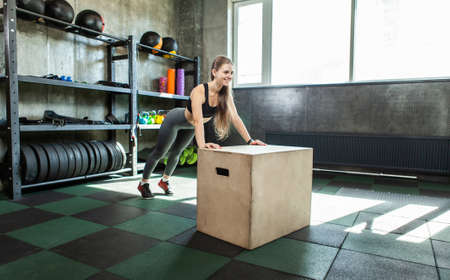 Beautiful slim young sports woman doing push ups on fitness box at gymの写真素材