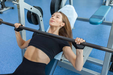 Young fit slim woman in sportswear trains pectoral muscles doing incline press in the gymの写真素材