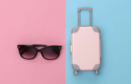 travel concept. Mini plastic travel suitcase and sunglasses on pink blue pastel background. minimal style. Top view, flat layの写真素材