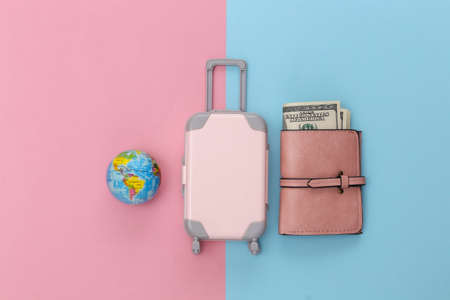 travel concept. Mini plastic travel suitcase, globe and purse on pink blue pastel background. minimal style. Top view, flat layの写真素材