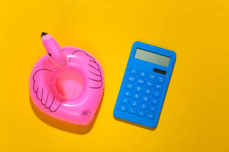 Inflatable pink flamingo with calculator on yellow sunny background. Summer vacation concept. minimalism. top view.の写真素材