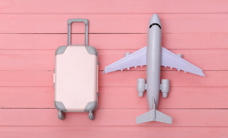 Flat lay vacation holiday and travel planning concept. Mini plastic travel suitcase and air plane on pink wooden background. top viewの写真素材
