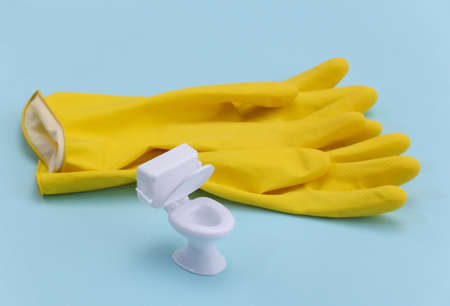 Cleaning in the restroom. Mini figure of a toilet with yellow rubber gloves on a blue backgroundの写真素材
