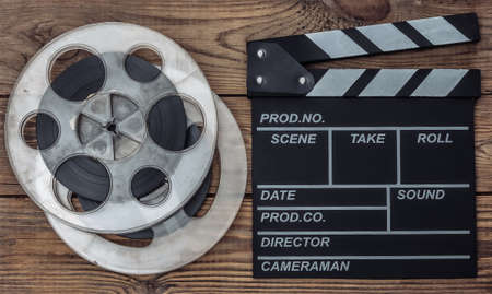Movie clapper board and film reel on wooden background. Cinema industry, entertainment. top viewの写真素材