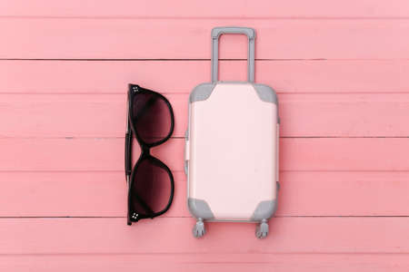 Flat lay vacation holiday and travel planning concept. Mini plastic travel suitcase and sunglasses on pink wooden background. top viewの写真素材