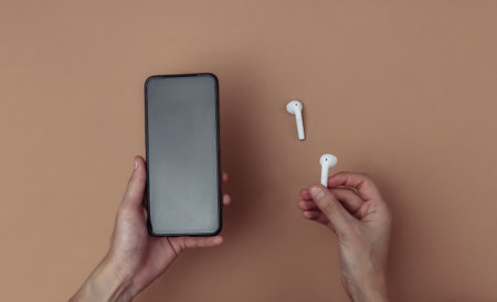 Woman holding a smartphone and wireless headphones on brown background. connection, synchronization. top viewの写真素材