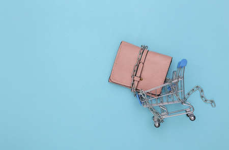 Mini shopping cart and wallet wrapped in a steel chain on blue background. top viewの写真素材
