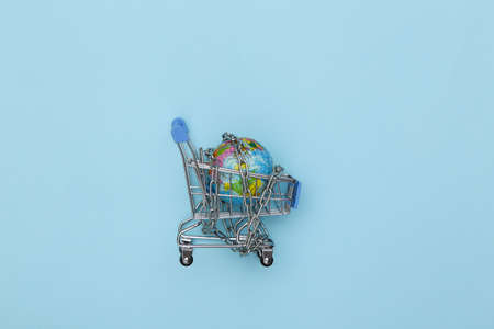 Mini shopping cart and globe wrapped in a steel chain on blue background. top view