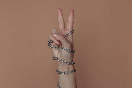 V fingers gesture, hand wrapped in a metal chain on a brown background. Suppression of freedom or imprisonmentの写真素材