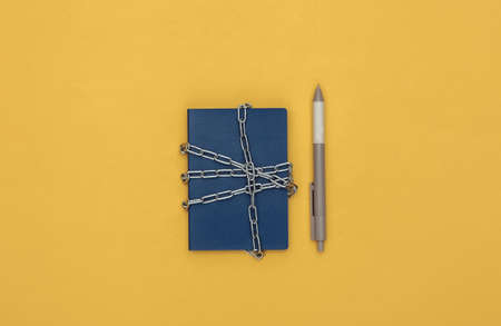 Passport wrapped in a metal chain and pen on a yellow background. top viewの写真素材