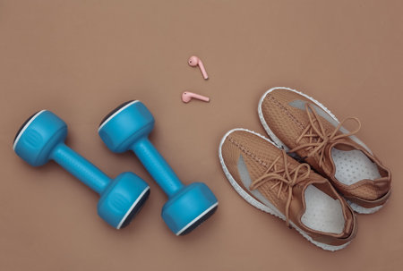 Dumbbells, textile sports shoes and wireless headphones on brown background. Fitness flat lay. top viewの写真素材