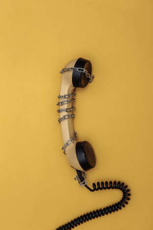 Telephone receiver wrapped in a steel chain on a yellow background. top viewの写真素材