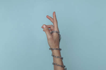 The hand wrapped in a metal chain on a blue background. Suppression of freedom or imprisonment, hostageの写真素材