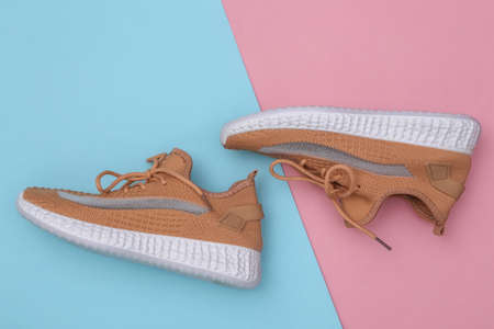 Brown textile sports shoes on a blue-pink pastel background. top view