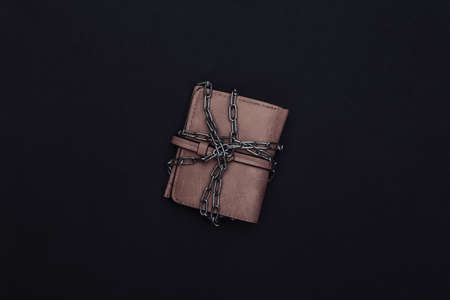 Leather wallet wrapped in a steel chain on black background.の写真素材