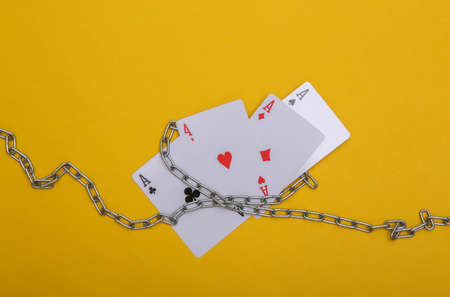 Four aces wrapped in a steel chain on yellow background. Prohibition of gambling business, casinosの写真素材