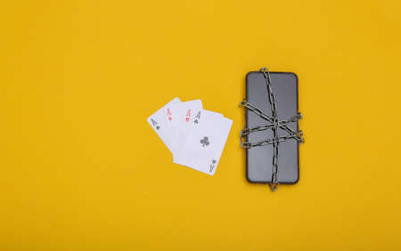 Four aces with smartphone wrapped in a steel chain on yellow background. Online casino banの写真素材