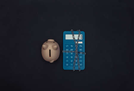 Blue calculator wrapped in steel chain and piggy bank on black background. top viewの写真素材