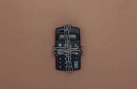 Calculator wrapped in steel chain on a brown background. top viewの写真素材