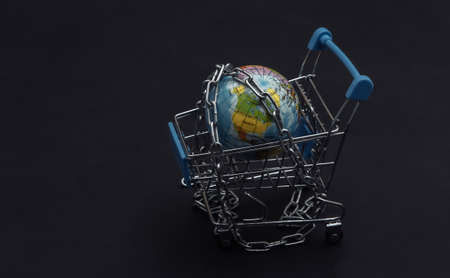 Mini shopping cart and globe wrapped in a steel chain on black backgroundの写真素材