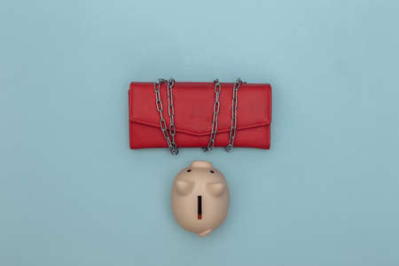 Leather wallet wrapped in a steel chain and piggy bank on blue background. top view