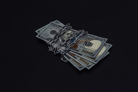 Hundred dollar bills wrapped in steel chain on black backgroundの写真素材