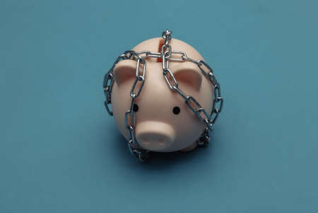 Piggy bank wrapped in steel chain on blue backgroundの写真素材