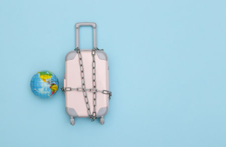 Mini travel baggage wrapped in steel chain and globe on blue background. Travel ban. top viewの写真素材