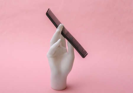 Mannequin hand holding comb on pink background. minimalism beauty conceptの写真素材