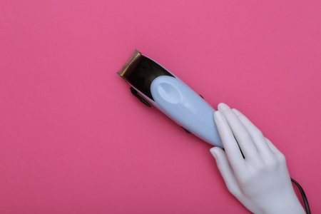 White hand of a mannequin holding a hair clipper on a pink background. beauty and fashionの写真素材