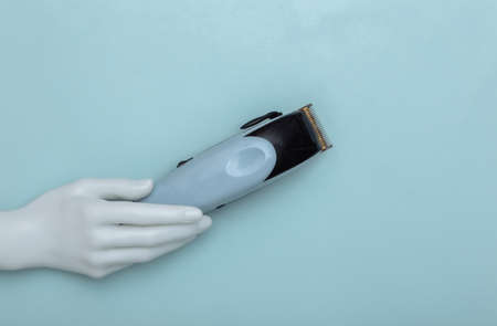 White mannequin hand holding a hair clipper on blue pastel background. beauty and fashion. top viewの写真素材