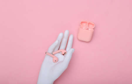 Menequin's white hand holds pink wireless headphones and charging case against pink pastel...