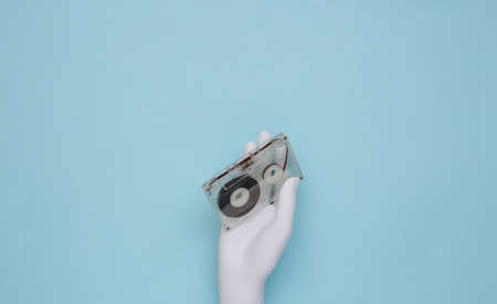 Mannequin's white hand holding retro audio cassette on blue background. top viewの写真素材