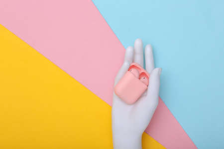 Menequin's white hand holds pink wireless headphones and charging case on colorful pastel background. minimalism. top viewの写真素材