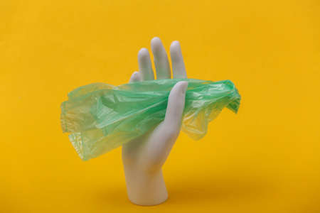 White mannequin hand hold plastic bag on yellow background. environmental pollution. Eco conceptの写真素材