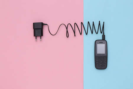 Push-button telephone with a charging adapter on blue pink background. top viewの写真素材