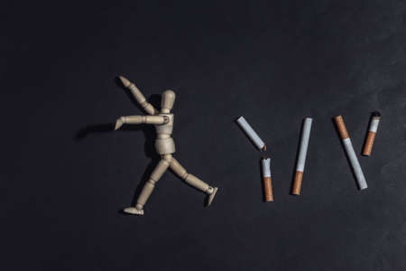 Wooden puppet runs from cigarettes on black background. Quitting smoking concept