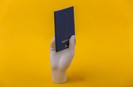 White mannequin hand holding passport on yellow background.
