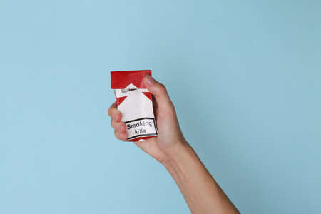 Hand holds crumpled pack of cigarettes on blue background