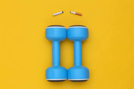 Sports vs bad habits. Dumbbell and broken cigarette on a yellow background. Quitting smokingの写真素材