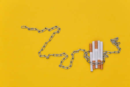 Steel chain wrapped cigarettes on a yellow background.の写真素材