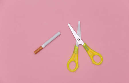 Scissors and a cigarette on a pink pastel background. top viewの写真素材