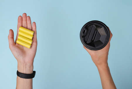 Hand holds batteries and a cup of coffee on a blue background. Recharge with energy!