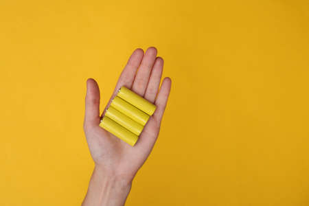 Hands holding aa type battery on yellow backgroundの写真素材