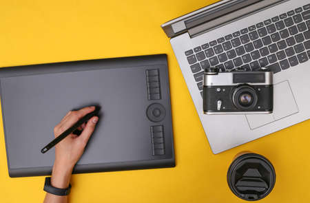Woman photographer or retoucher working with graphic tablet, camera and laptop on yellow backgroundの写真素材