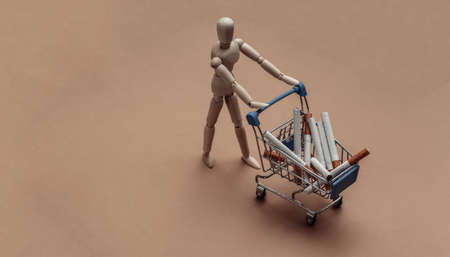 Puppet rolls mini supermarket trolley with cigarettes on brown backgroundの写真素材