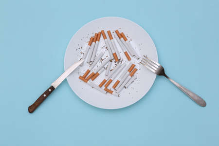 Many cigarettes in plate with fork and knife on blue background. top viewの写真素材
