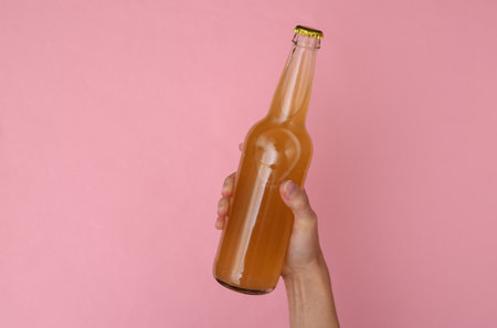 Hand holds a bottle of beer on a pink background