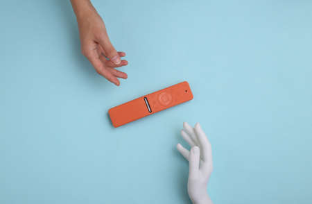Human and mannequin hand touching tv remote on blue background