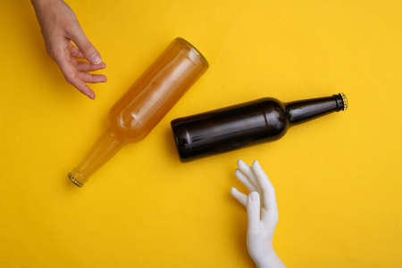 Human and mannequin hand touching beer bottle on yellow backgroundの写真素材